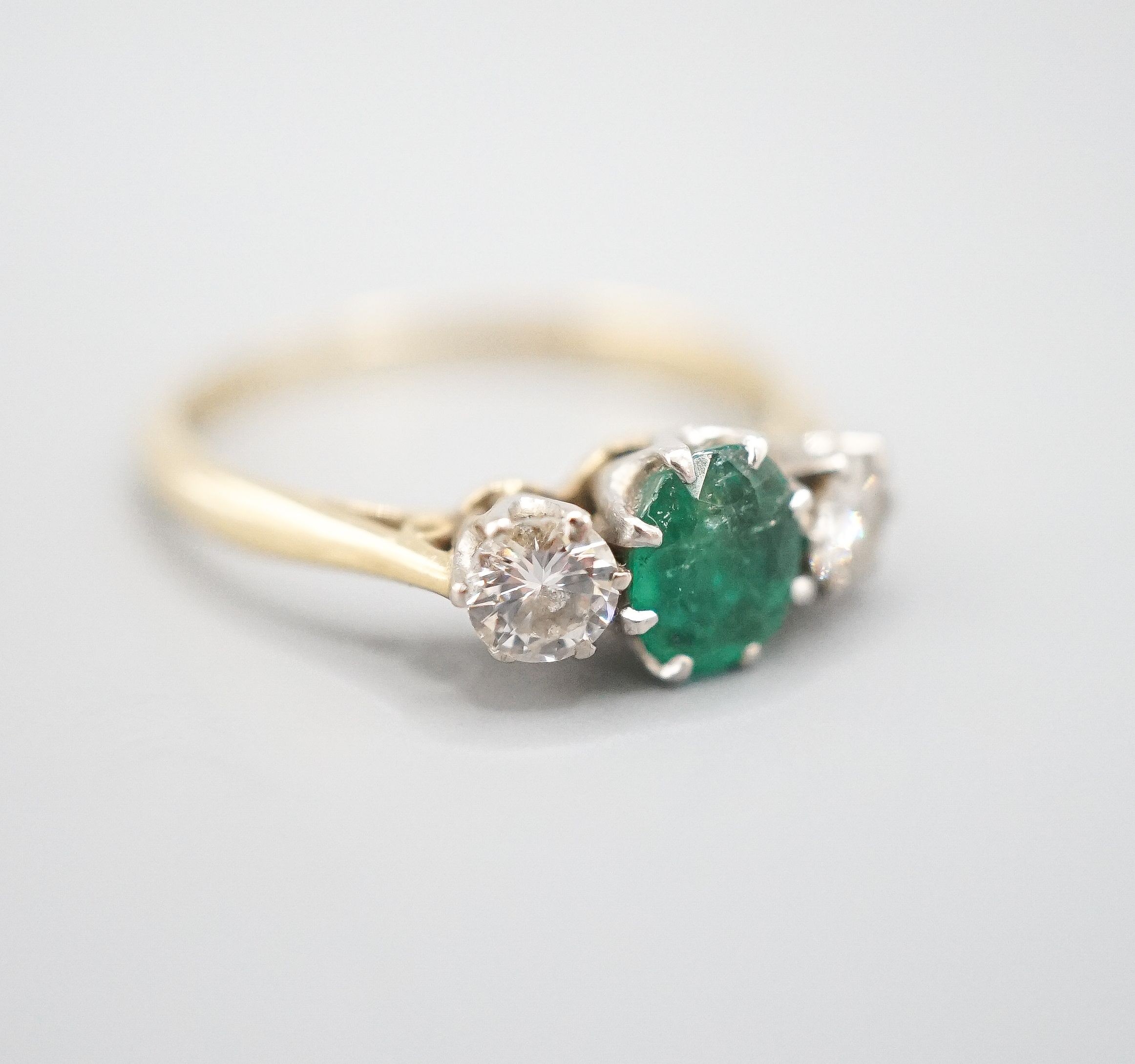 An 18ct and plat, emerald and diamond set three stone ring, size K, gross weight 2.3 grams.